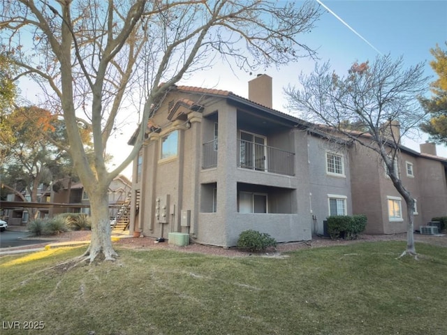 view of side of property featuring a balcony, central air condition unit, and a lawn