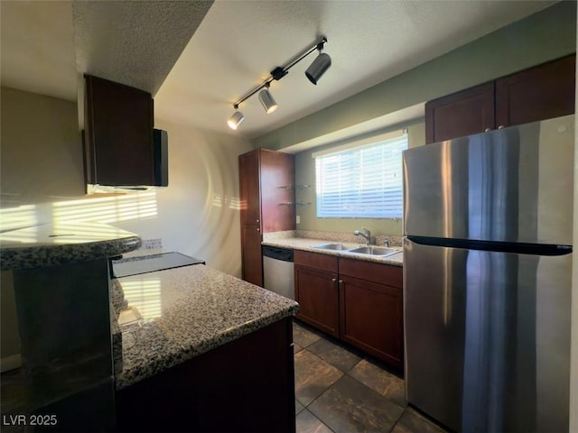 kitchen with appliances with stainless steel finishes, a textured ceiling, rail lighting, sink, and light stone counters