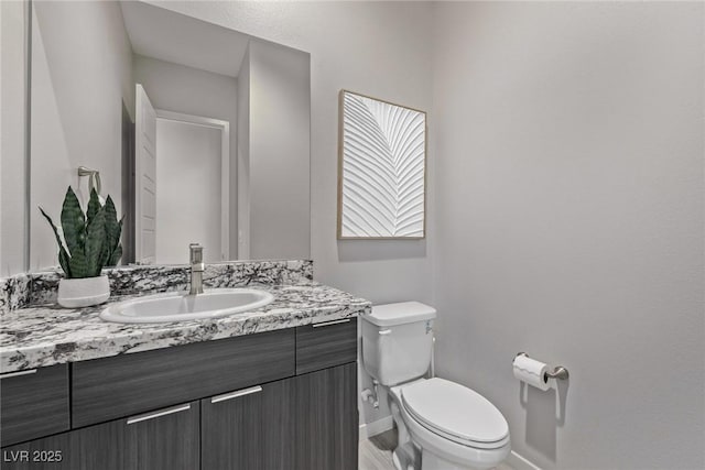 half bath with baseboards, vanity, and toilet