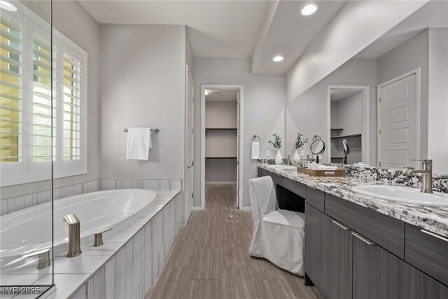 full bath with a garden tub, double vanity, a spacious closet, a sink, and baseboards