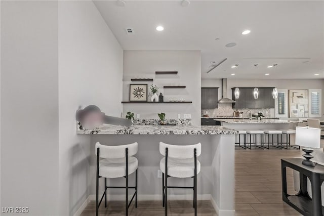 kitchen featuring tasteful backsplash, visible vents, a breakfast bar area, hanging light fixtures, and wall chimney range hood