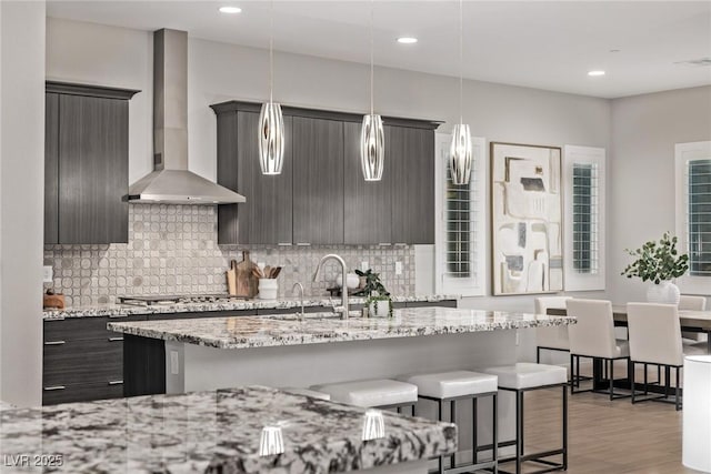 kitchen featuring a breakfast bar area, stainless steel gas cooktop, backsplash, and wall chimney exhaust hood