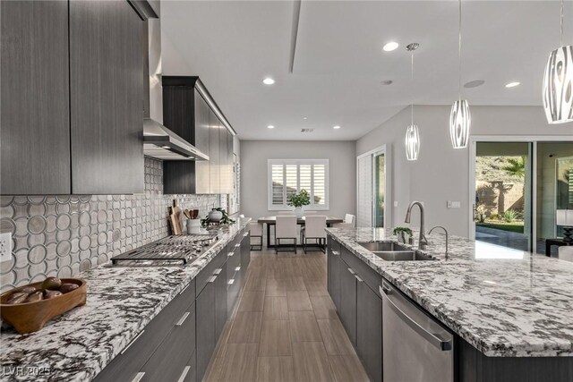 kitchen with a large island, backsplash, appliances with stainless steel finishes, a sink, and wall chimney exhaust hood