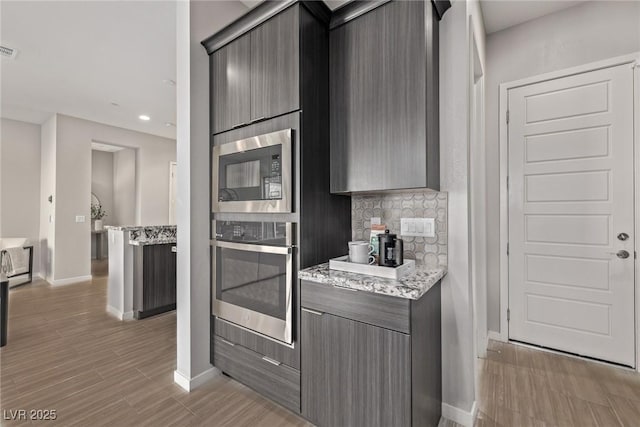 kitchen featuring visible vents, baseboards, appliances with stainless steel finishes, decorative backsplash, and light stone countertops