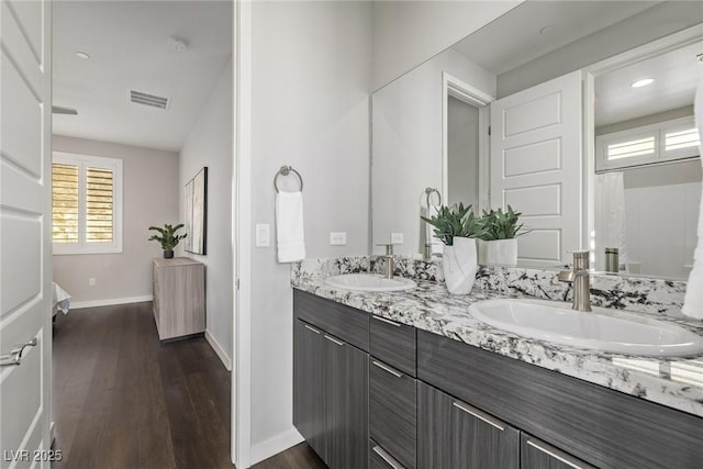 full bath with double vanity, a sink, baseboards, and wood finished floors