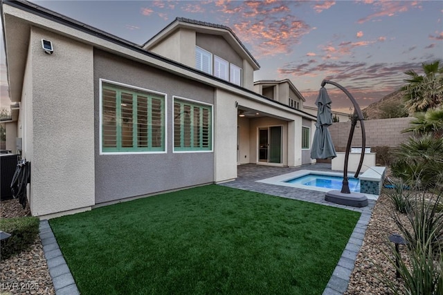 rear view of house with a fenced backyard, a lawn, a jacuzzi, and stucco siding