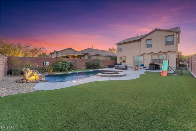 pool at dusk featuring an in ground hot tub, pool water feature, a lawn, and an outdoor fire pit