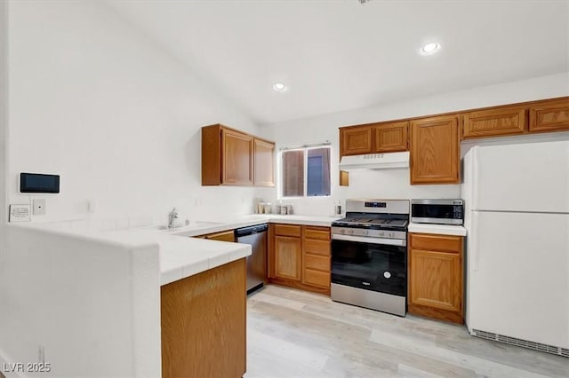 kitchen with stainless steel appliances, sink, kitchen peninsula, vaulted ceiling, and light hardwood / wood-style flooring