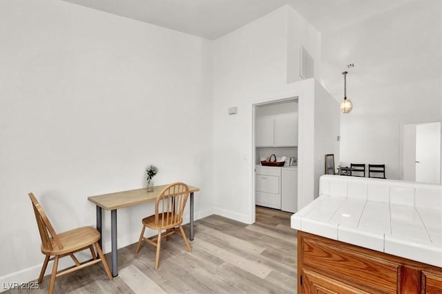 kitchen featuring light hardwood / wood-style flooring, washing machine and dryer, hanging light fixtures, and tile counters