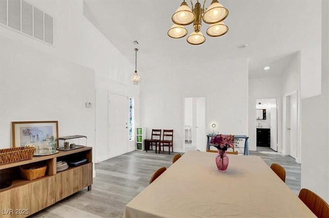 dining room featuring high vaulted ceiling, light hardwood / wood-style flooring, and a notable chandelier