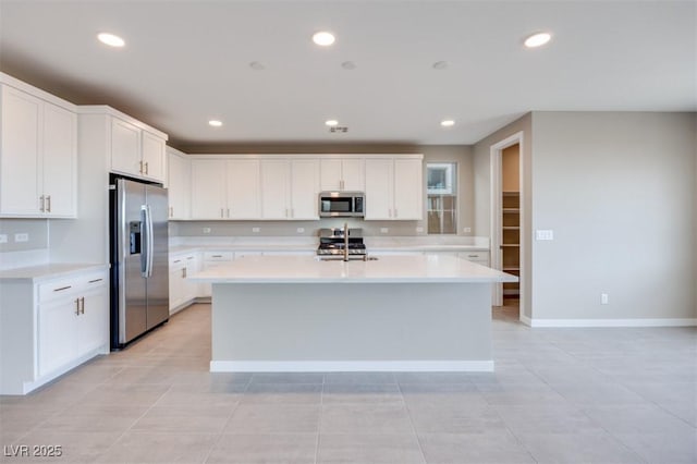 kitchen with stainless steel appliances, light tile patterned floors, a center island with sink, and white cabinets