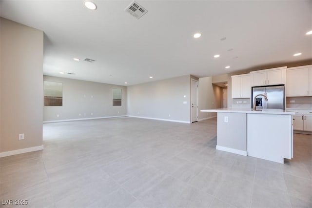 kitchen featuring stainless steel refrigerator with ice dispenser, a kitchen island with sink, and white cabinets