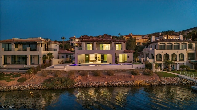 back house at dusk with a pool, a water view, and a patio area