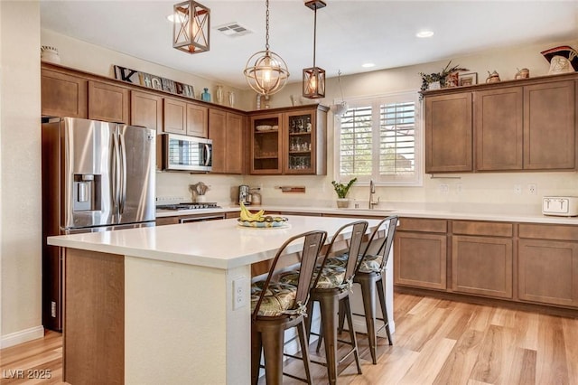 kitchen featuring light hardwood / wood-style floors, appliances with stainless steel finishes, a kitchen breakfast bar, a kitchen island, and pendant lighting