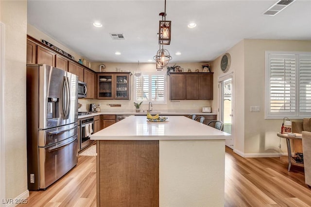 kitchen with appliances with stainless steel finishes, hanging light fixtures, sink, a kitchen island, and light hardwood / wood-style flooring