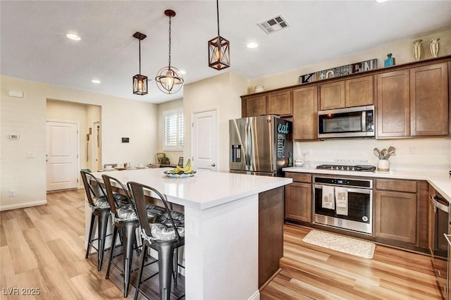 kitchen featuring a kitchen island, stainless steel appliances, hanging light fixtures, light hardwood / wood-style flooring, and a breakfast bar area