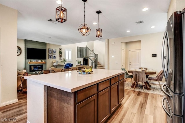 kitchen featuring hanging light fixtures, light hardwood / wood-style flooring, a center island, and stainless steel refrigerator