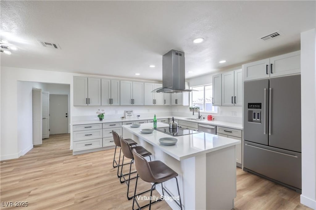 kitchen with a kitchen island, appliances with stainless steel finishes, sink, a kitchen bar, and island exhaust hood