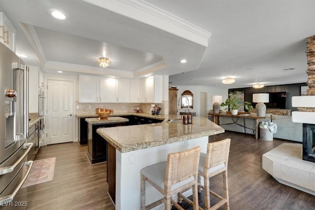 kitchen with high end fridge, a kitchen breakfast bar, kitchen peninsula, white cabinets, and a raised ceiling