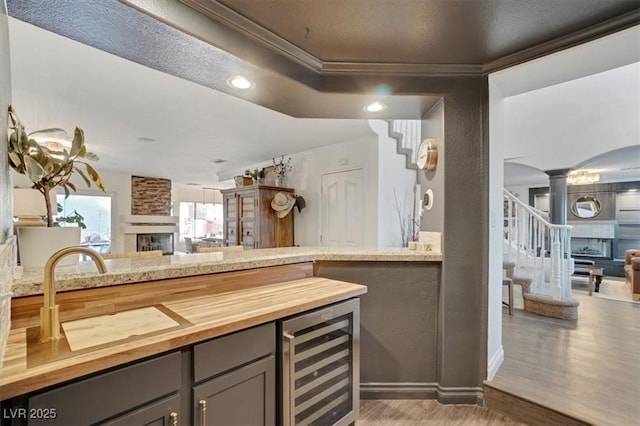 kitchen featuring wine cooler, wood-type flooring, ornamental molding, a fireplace, and decorative columns