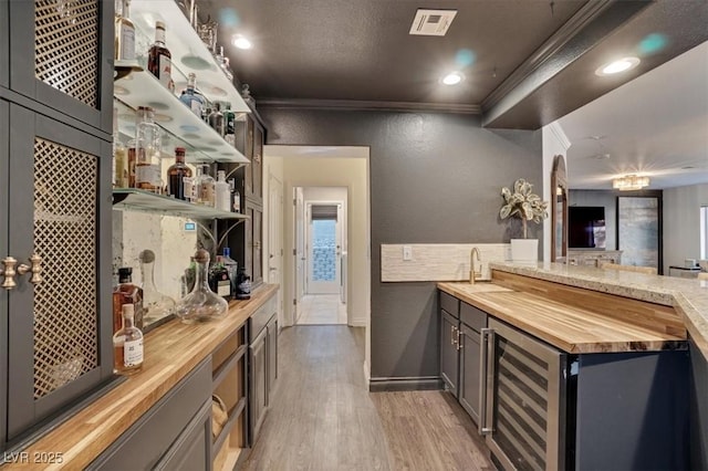 bar featuring butcher block countertops, wood-type flooring, sink, beverage cooler, and crown molding