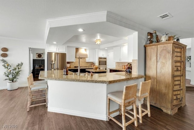 kitchen featuring stainless steel appliances, white cabinetry, light stone countertops, and kitchen peninsula