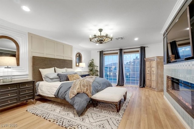 bedroom featuring a tiled fireplace, crown molding, light hardwood / wood-style floors, and a chandelier