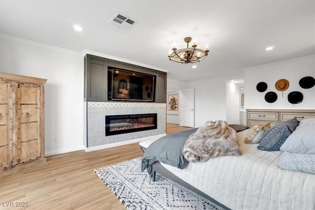 bedroom featuring a tiled fireplace, crown molding, an inviting chandelier, and light hardwood / wood-style flooring