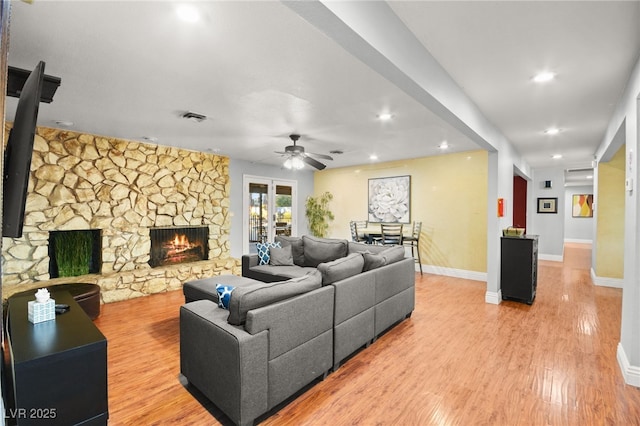 living room featuring ceiling fan, light hardwood / wood-style flooring, and a stone fireplace