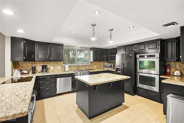 kitchen with hanging light fixtures, black appliances, a center island, and a raised ceiling