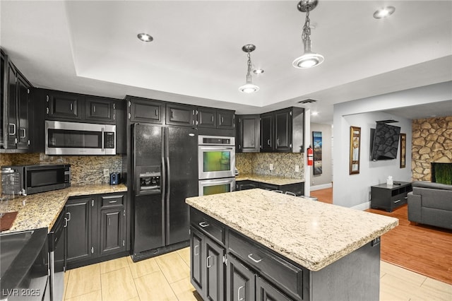 kitchen with a center island, appliances with stainless steel finishes, pendant lighting, backsplash, and light stone counters