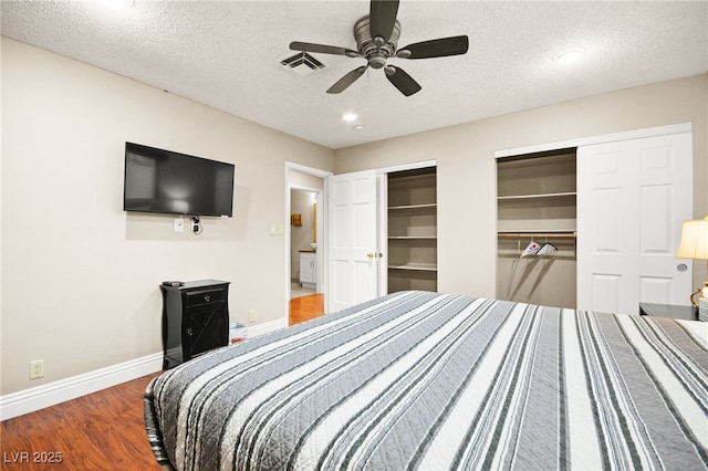 bedroom with ceiling fan, two closets, a textured ceiling, and hardwood / wood-style flooring