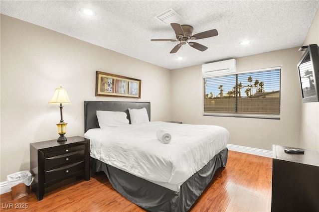 bedroom with wood-type flooring, a textured ceiling, an AC wall unit, and ceiling fan