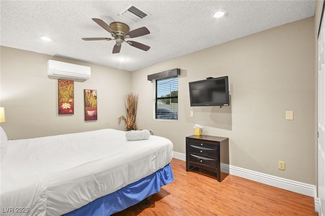 bedroom with light wood-type flooring, ceiling fan, a textured ceiling, and a wall unit AC