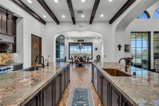 kitchen featuring dark brown cabinetry, light stone counters, pendant lighting, and a sink