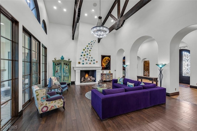 living area featuring a warm lit fireplace, dark wood-style flooring, a towering ceiling, and beam ceiling