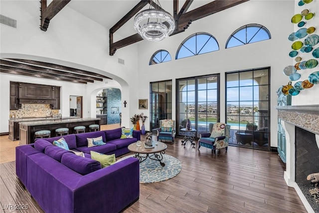 living room with a towering ceiling, a fireplace, beamed ceiling, a chandelier, and hardwood / wood-style flooring