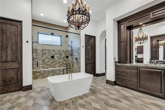 bathroom featuring baseboards, a tile shower, a freestanding bath, vanity, and a notable chandelier