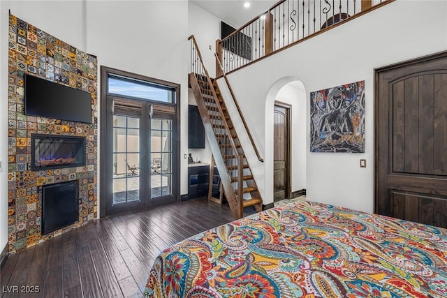 bedroom featuring arched walkways, dark wood-type flooring, a fireplace, a towering ceiling, and access to outside