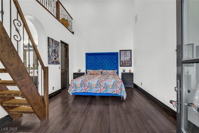 bedroom with dark wood-type flooring, a towering ceiling, and baseboards