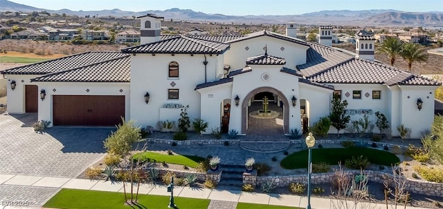 mediterranean / spanish house featuring an attached garage, a tile roof, a mountain view, and decorative driveway