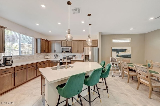 kitchen with pendant lighting, appliances with stainless steel finishes, tasteful backsplash, a kitchen bar, and a center island with sink