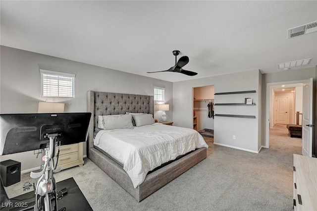 bedroom featuring a walk in closet, ceiling fan, light carpet, and a closet