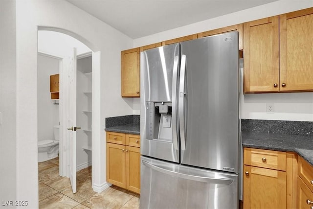 kitchen featuring stainless steel fridge, dark stone counters, and light tile patterned flooring