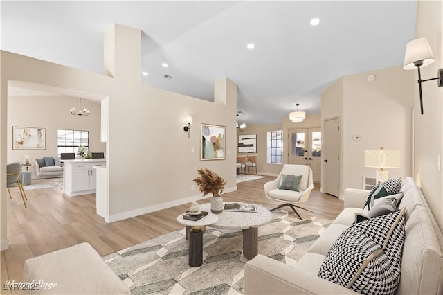 living room featuring french doors, a towering ceiling, light hardwood / wood-style flooring, and a notable chandelier