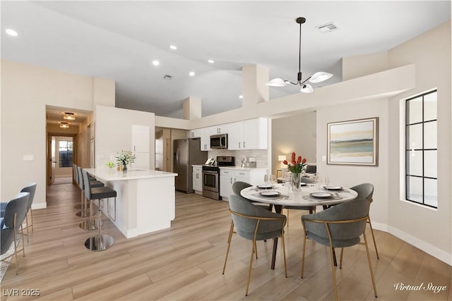 dining area featuring light hardwood / wood-style flooring, high vaulted ceiling, and a chandelier