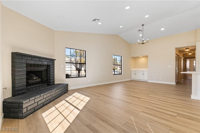 unfurnished living room featuring a notable chandelier, a fireplace, light hardwood / wood-style floors, and vaulted ceiling