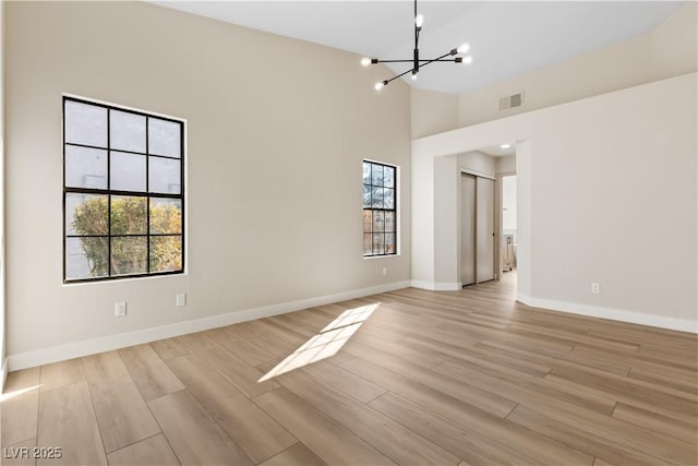 spare room with high vaulted ceiling, a chandelier, and light hardwood / wood-style floors