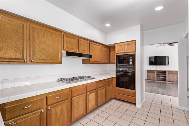 kitchen with black appliances, ceiling fan, light tile patterned floors, and tile countertops