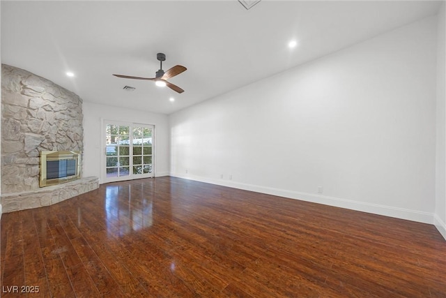 unfurnished living room featuring ceiling fan, a stone fireplace, and dark hardwood / wood-style flooring